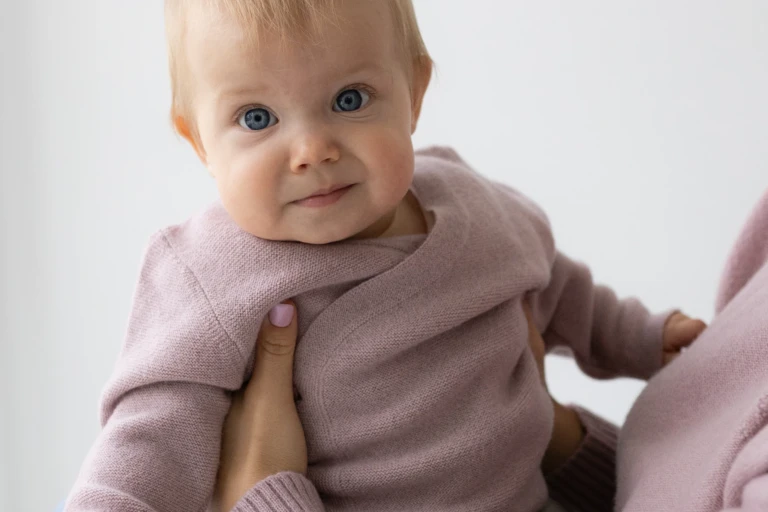 Niemowlę w różowym kardiganie z wełny merino podtrzymywane przez mamę