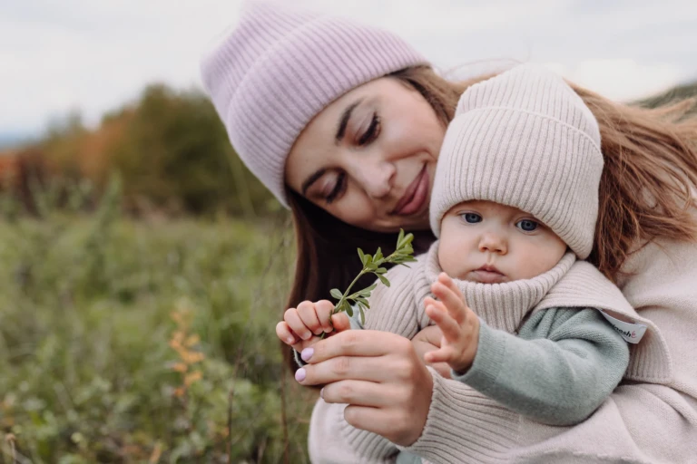 Mama i niemowlę w czapkach z wełny merino oglądają gałązkę na jesiennej łące