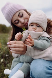 Mama w różowej czapce i niemowlę w beżowej czapce merino niemowlęcej oglądają gałązkę