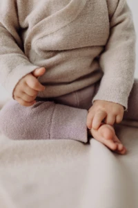 Dłonie i stópki niemowlęcia w beżowym kardiganie merino dziecięcym z bliska