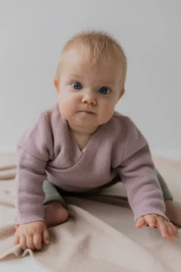 Niemowlę w różowym kardiganie raczkuje po beżowym kocyku merino na jasnym tle