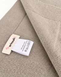 Róg beżowego kocyka merino z metką Merinoshe i wszywką z symbolami prania