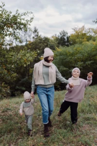 Mama biegnie przez łąkę z dwójką dzieci, chłopiec w beżowym kominie merino dziecięcym