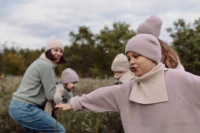 Chłopiec w beżowym kominie merino dziecięcym z rozłożonymi rękami bawi się na łące z rodziną