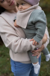 Mama w jasnym swetrze tuli niemowlę w beżowym kominie merino niemowlęcym w parku