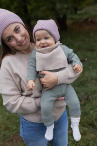 Mama i niemowlę w beżowym kominie merino niemowlęcym uśmiechają się do obiektywu w parku