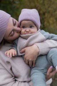 Mama całuje w policzek niemowlę w beżowym kominie merino niemowlęcym, zbliżenie