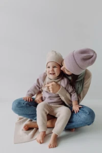 Mama całuje córkę w beżowych spodniach merino dziecięcych siedzącą jej na kolanach