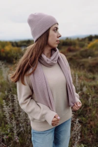 Kobieta w beżowym swetrze merino damskim i różowym szalu patrzy w bok na łące