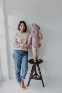 Mama w beżowym swetrze merino damskim stoi obok córki na drewnianym stołku