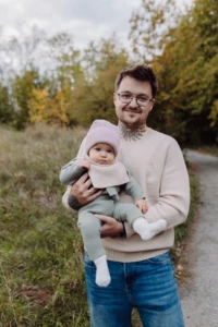 Mężczyzna w beżowym swetrze merino męskim z niemowlęciem na rękach na jesiennej ścieżce