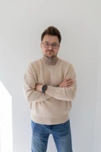 Mężczyzna w okularach w beżowym swetrze merino męskim ze skrzyżowanymi rękami