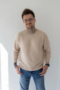 Mężczyzna w beżowym swetrze merino męskim z dłońmi w kieszeniach jeansów