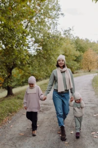 Mama w beżowym szalu merino spaceruje z dziećmi jesienną aleją wśród drzew